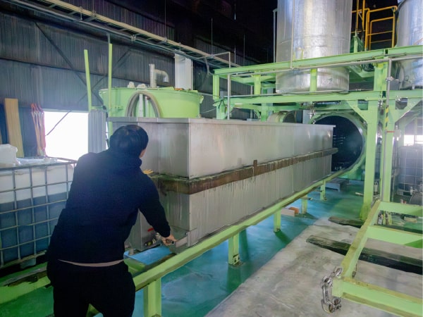 木材が詰まれた金属製のバットを押し込み、含浸装置に挿入する様子